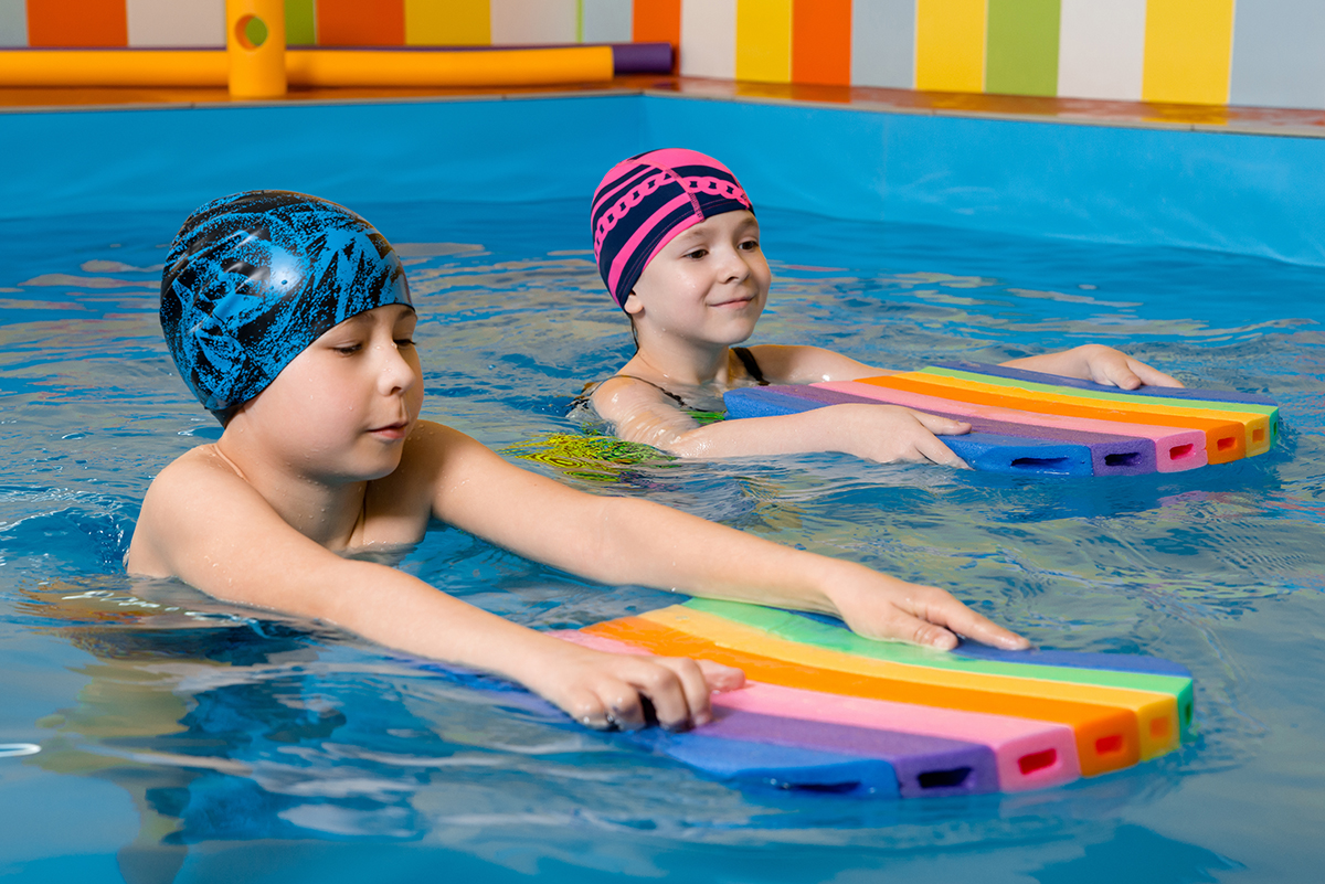 Boy and girl wearing a swimsuit uses a foam pad to practice swimming in a swimming pool